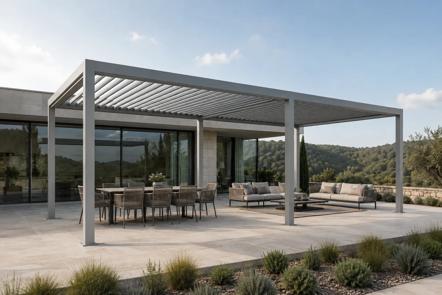 Grey aluminium louvered pergola over a terrace with separate dining and sofa areas facing a garden and wooded hills