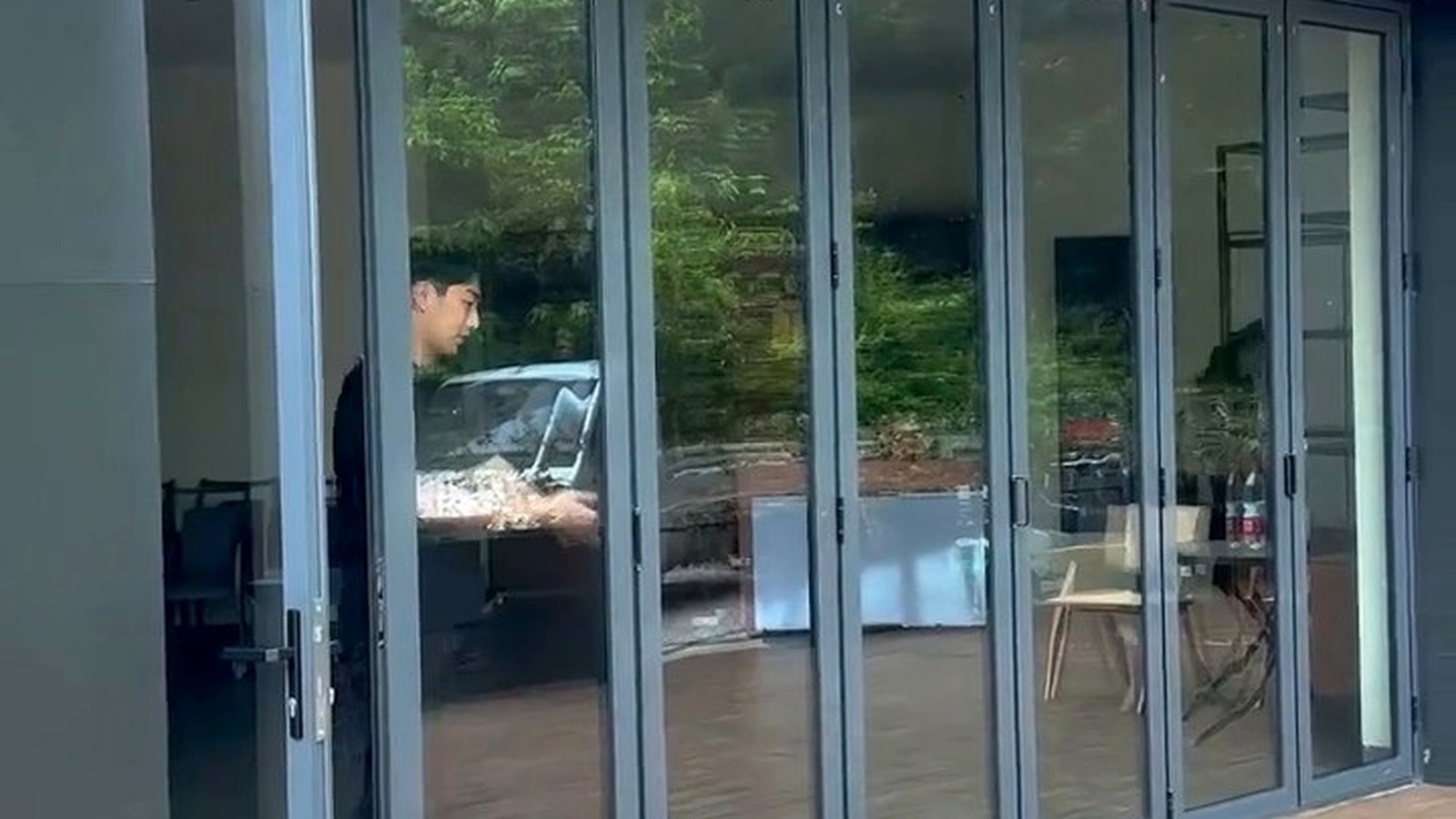 Grey-framed glazed folding doors with reflections of the room and greenery